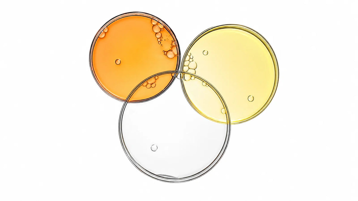 Three overlapping circular bubbles or droplets with orange, yellow, and clear liquid contents against a white background.