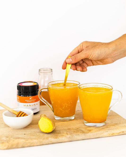hand stirring manuka honey immunity drink on chopping board next to ginger