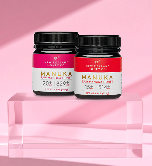 Two jars of Manuka honey on a pink background.