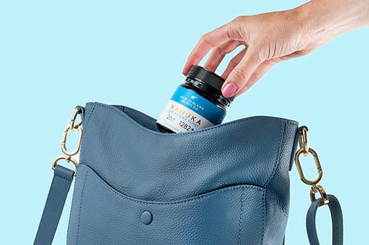Hand placing a jar into a blue handbag against a light blue background.