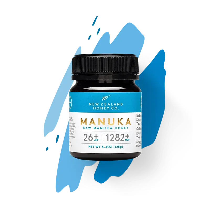New Zealand Honey Co. Manuka Honey Mini jar UMF™ 26+ MGO 1282+ (blue label) on a blue paint-splash studio background, 125g (4.4oz)