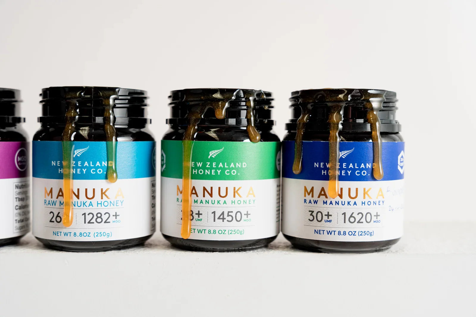 Three jars of New Zealand Honey Co. raw manuka honey with varying UMF ratings, displayed in a product line-up.