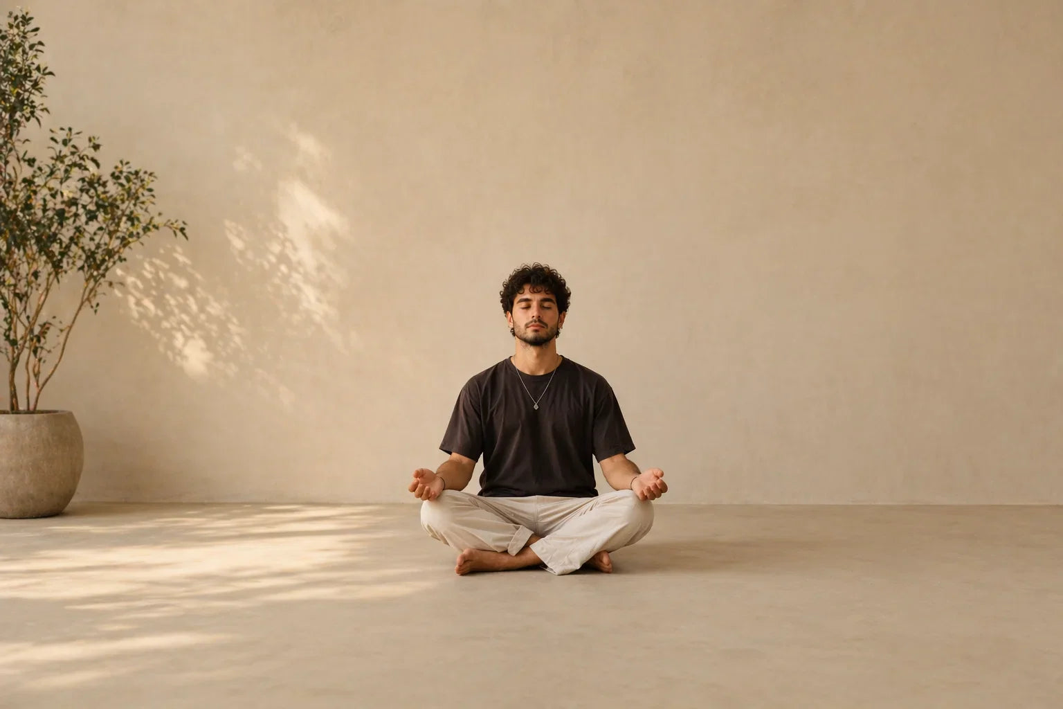 Man in meditation pose on light floor with neutral beige walls and potted plant