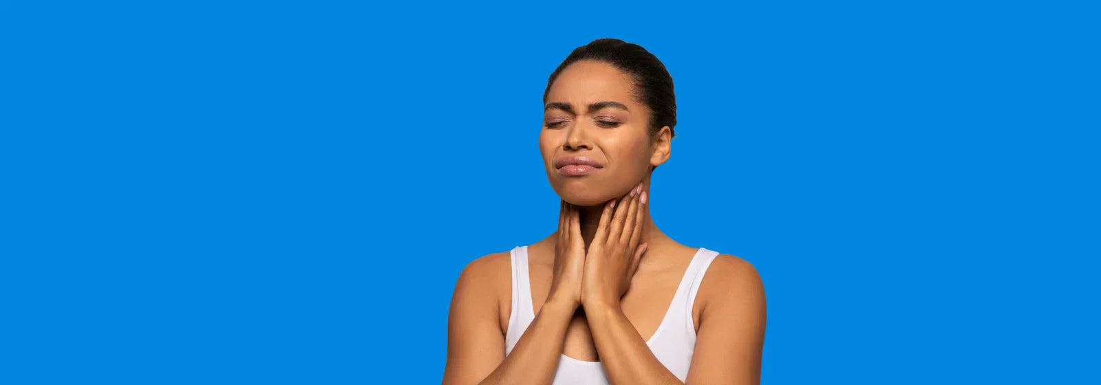 Woman touching her neck with eyes closed against a bright blue background, appearing uncomfortable or experiencing pain.