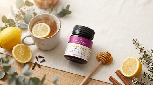 Manuka honey jar beside lemon tea, lemons, cloves, cinnamon, eucalyptus, and a honey dipper.