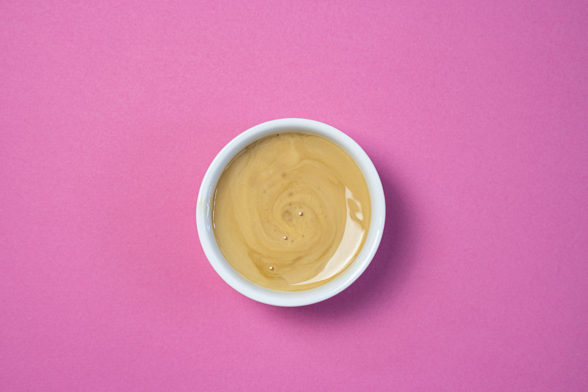 Bowl of creamy peanut butter on a pink background.