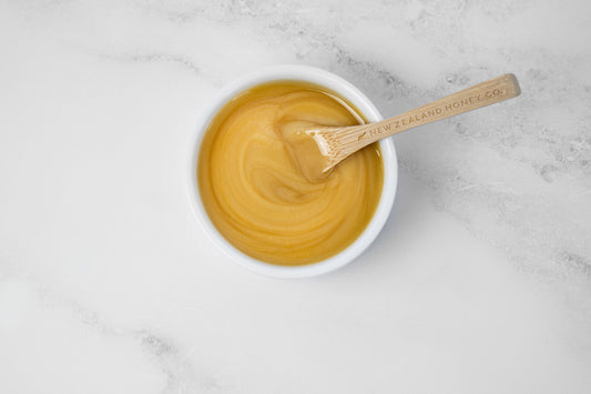Bowl of honey with a wooden spoon on a marble surface.