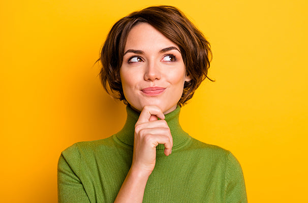 Woman in green top with thoughtful expression against yellow background.