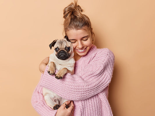 Woman hugging a pug dog against a light orange background.