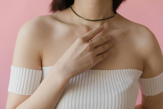 Person in off-shoulder top with a necklace against a pink background.