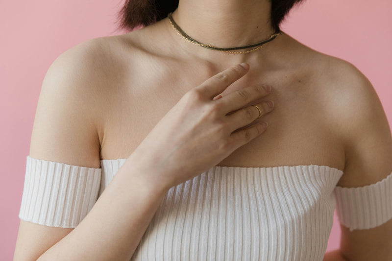 Person in off-shoulder top with a necklace against a pink background.