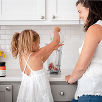 Mother and young daughter making a smoothie in a white kitchen, New Zealand Honey Co. Manuka Honey UMF™ 10+ on the counter