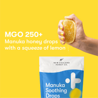 MGO 250+ Manuka honey drops with a squeeze of lemon — hand squeezing a lemon half above the New Zealand Honey Co. Manuka Soothing Drops pouch on a yellow background