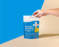 Hand holding the New Zealand Honey Co. Manuka Soothing Drops MGO 250+ Lemon pouch in front of a blue and cream split background