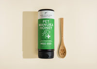 New Zealand Honey Co. Pet Manuka Honey MGO 550+ squeezy bottle for dogs and cats laid flat beside a bamboo paw-print spoon, 500g (17.6oz)