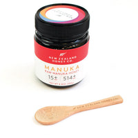 New Zealand Honey Co. bamboo Daily Spoon laid flat beside the brand's Manuka Honey UMF™ 15+ MGO 514+ jar on a white surface