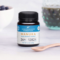 New Zealand Honey Co. Manuka Honey Mini jar UMF™ 26+ MGO 1282+ (blue label) on a kitchen surface beside a white wooden spoon, 125g (4.4oz)