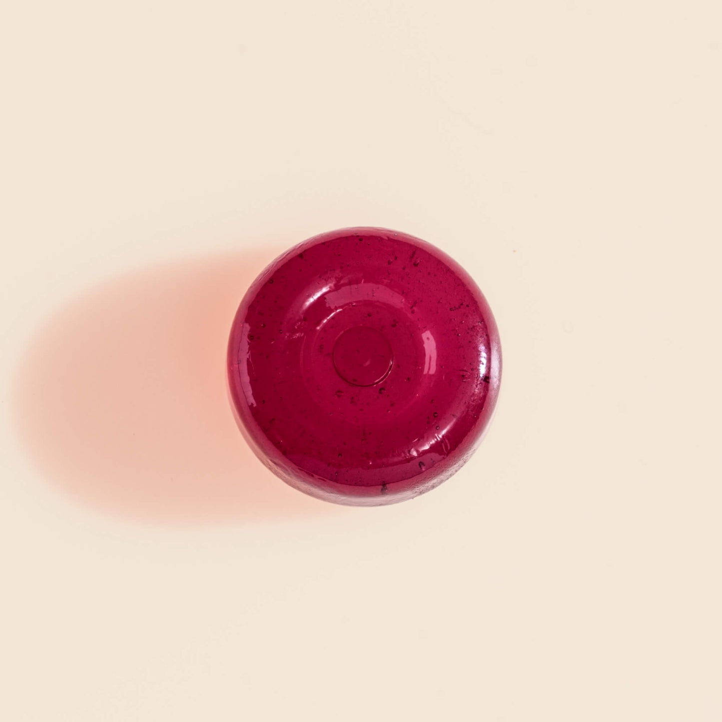 Close-up top-down view of a single deep-red Manuka Soothing Drop lozenge on a cream background