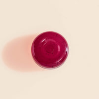 Close-up top-down view of a single deep-red Manuka Soothing Drop lozenge on a cream background